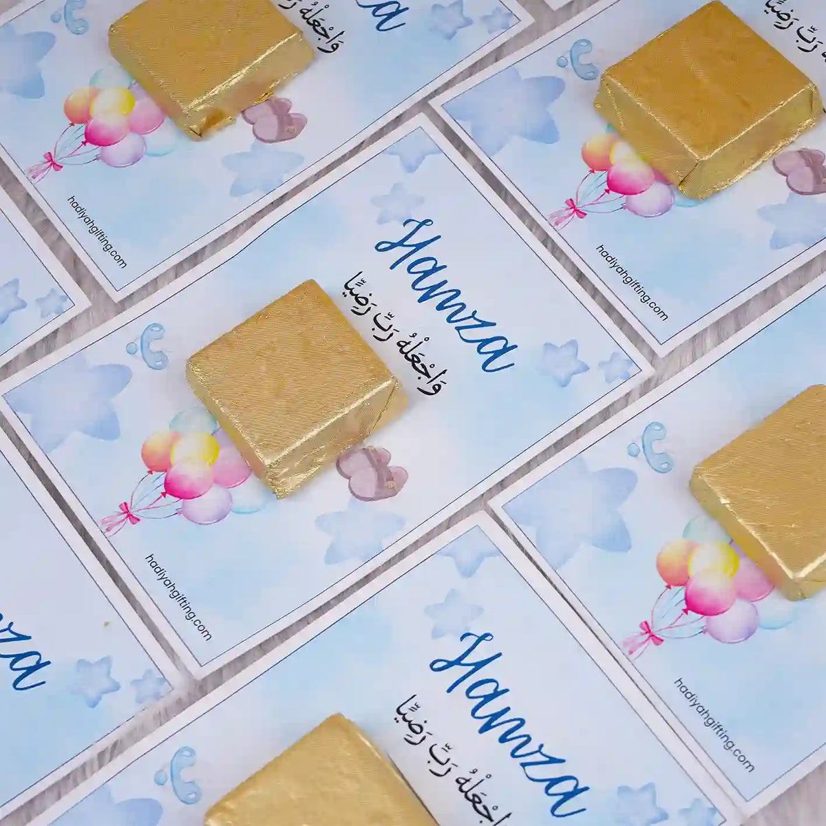 Aqiqah Sweet Blessings Favors with gold chocolates on blue custom cards labeled 'Hamza', ideal for baby boy Aqiqah celebrations.