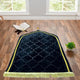 Black Dome Janamaz with golden border placed in a serene prayer setting with Quran and plant, enhancing spiritual ambiance.