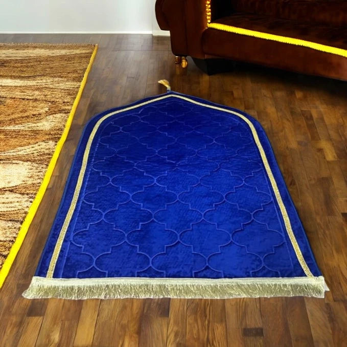 Dome-shaped Blue Janamaz with gold border and tassels on wooden floor, perfect for Hajj & Umrah gifts and daily prayers.