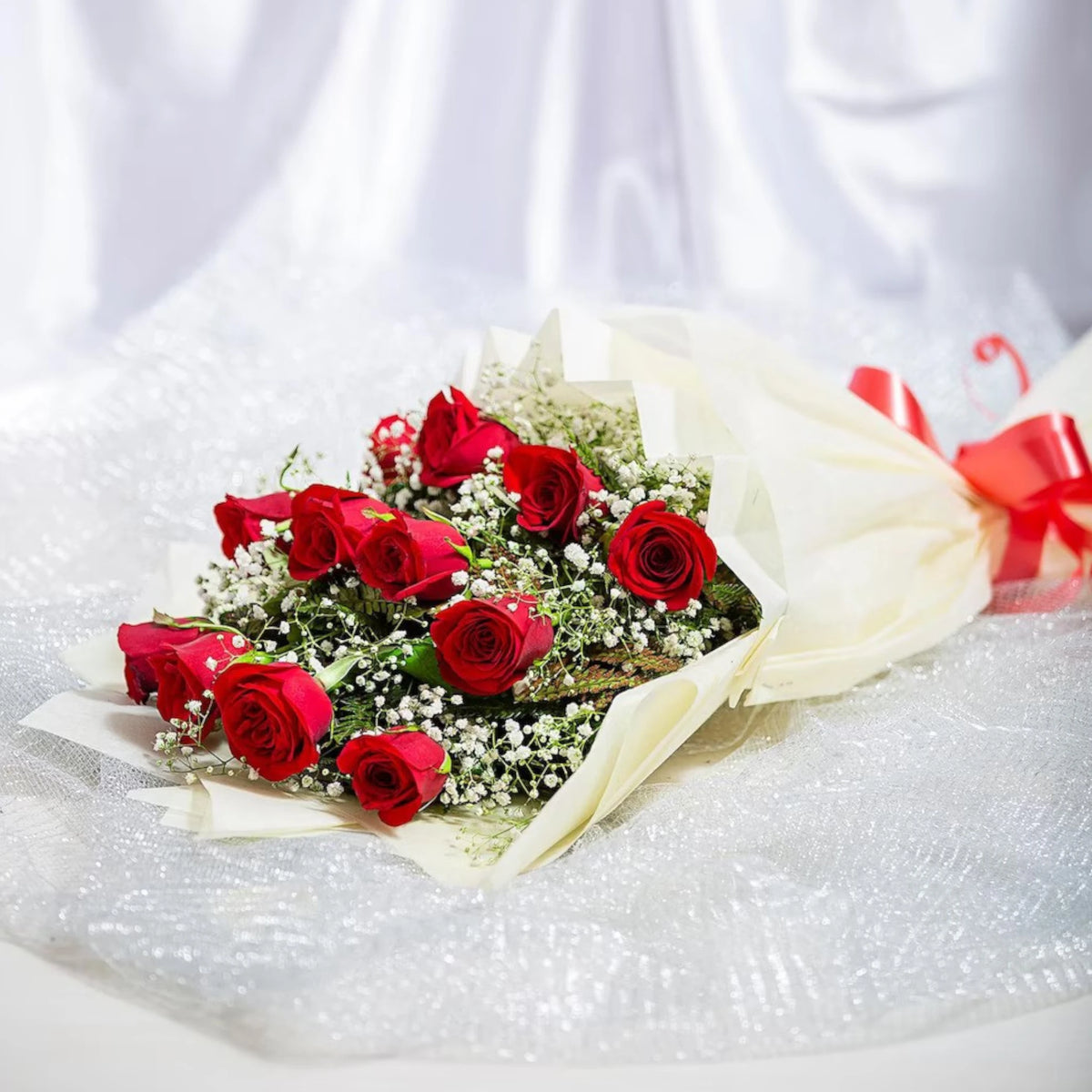 Classic Aura 12 Red Roses Bouquet - Perfect Gift laid flat, showcasing red roses with green and white fillers in soft cream wrapping and red ribbon.