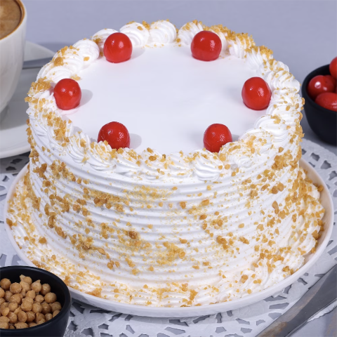 A round butterscotch cake with white frosting, butterscotch crumbs covering the sides, and a ring of whipped cream swirls topped with red cherries on a white plate. Main image