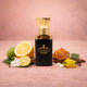 A bottle of Arba Warbat Attar perfume, a black and gold bottle with a textured gold cap, surrounded by fresh ingredients like limes, jasmine, ylang-ylang, and amber resin, on a soft pink background.