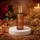 Omour Al Shaikh perfume bottle with gold cap on marble stand, floral and candle background