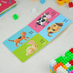 Educational card with animal illustrations and Arabic text on a white surface with toys around.