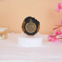 Black 3" Ayatul Kursi Frame with golden flakes, perfect for Ramadan & EID decorations or gifting. Set on a white base with pink flowers nearby.