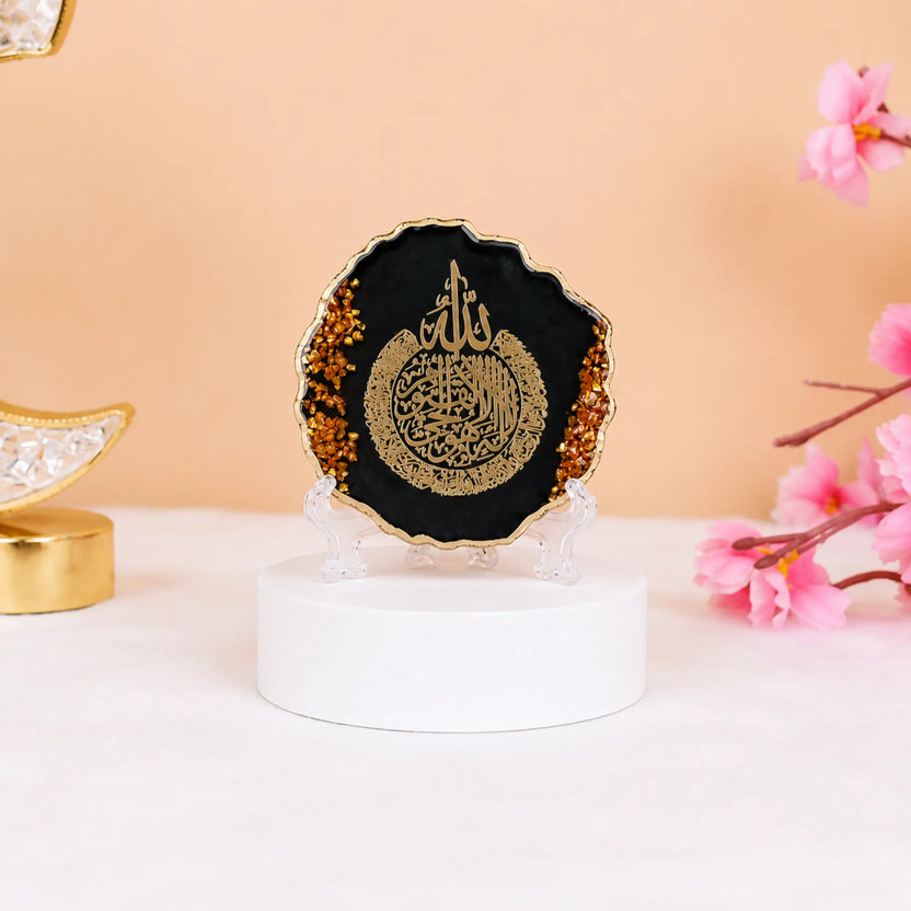 Black 3" Ayatul Kursi Frame with golden flakes, perfect for Ramadan & EID decorations or gifting. Set on a white base with pink flowers nearby. Main image