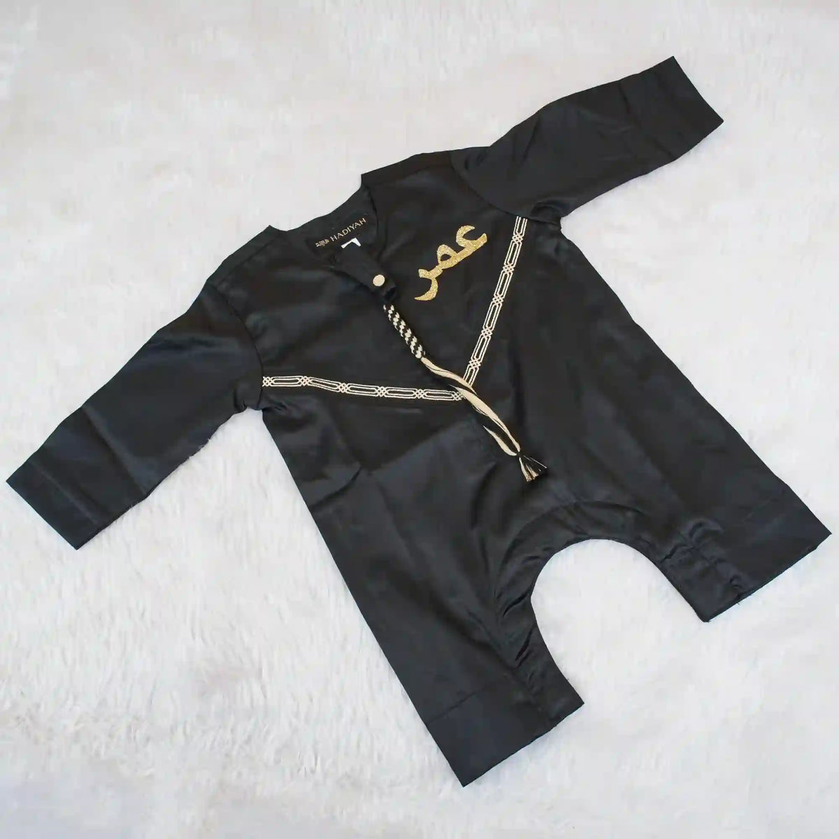 Flat lay of Black Thobe Romper for Babies featuring soft fabric, gold detailing, and snap-button design for easy wear.