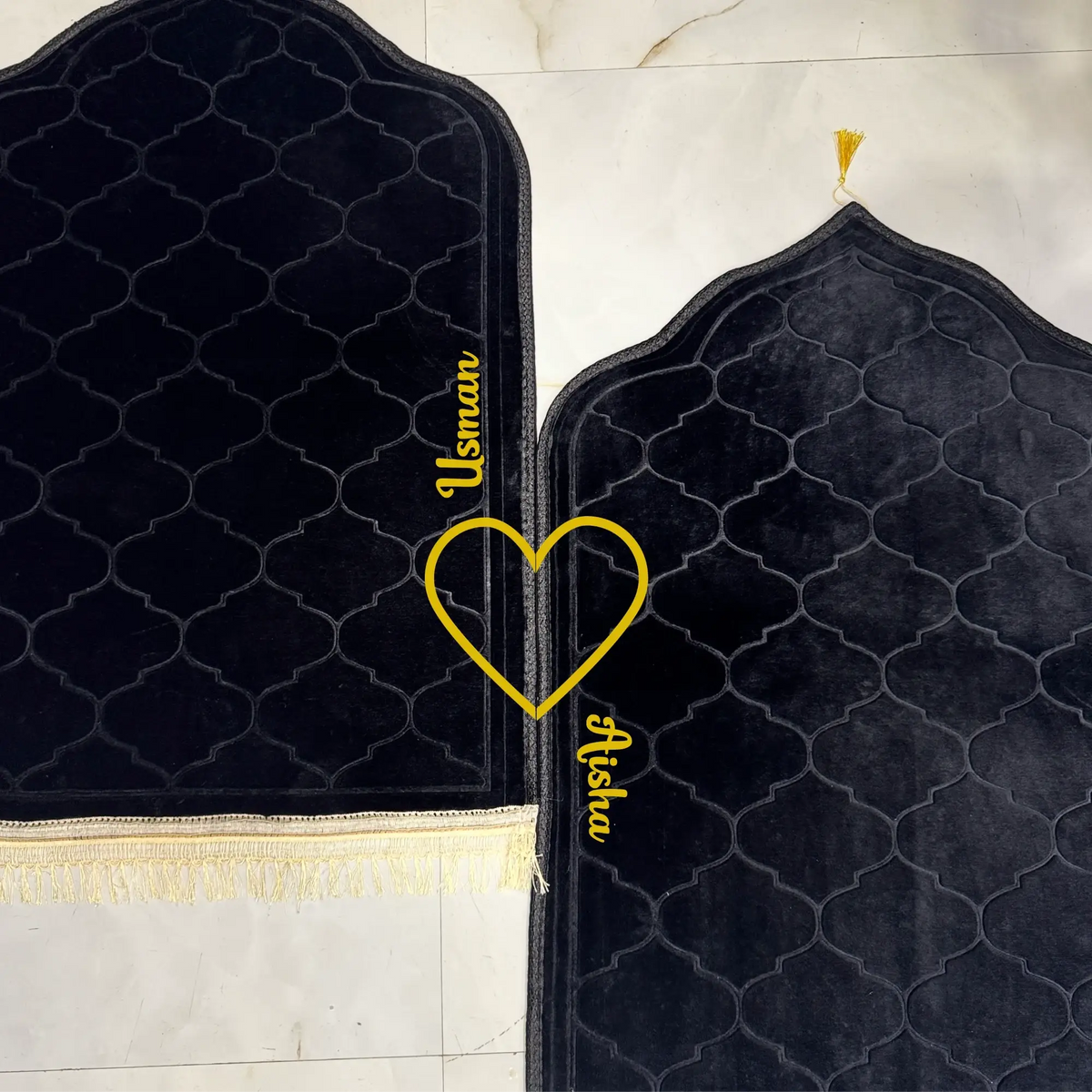 Two black prayer mats with gold embroidery on a marble floor.
