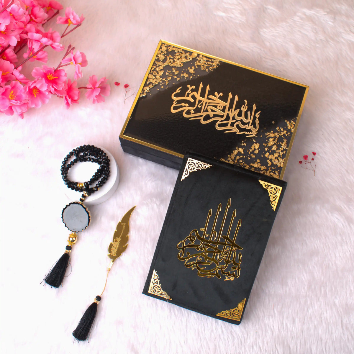 Black and gold decorative items with Arabic calligraphy on a white surface with pink flowers.