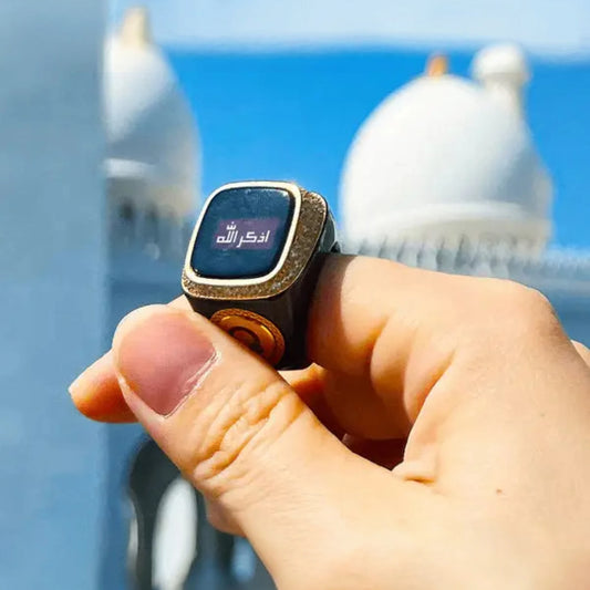 Zikr Ring with 99 Zirconia held against mosque backdrop, displaying Arabic text on screen. Elegant Islamic accessory for devotion and prayer.