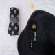 A black-themed Women's Namaz Essentials Hamper flat lay, showcasing a rolled patterned prayer dress, a black velvet prayer mat, a black mini velvet Quran box, black tasbeeh beads, and a digital counter.