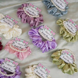 Assorted silk scrunchies with custom floral cards from Noor Bridal Pearl & Silk Favors – elegant satin favors with pearl bracelets for bridal shower and wedding events