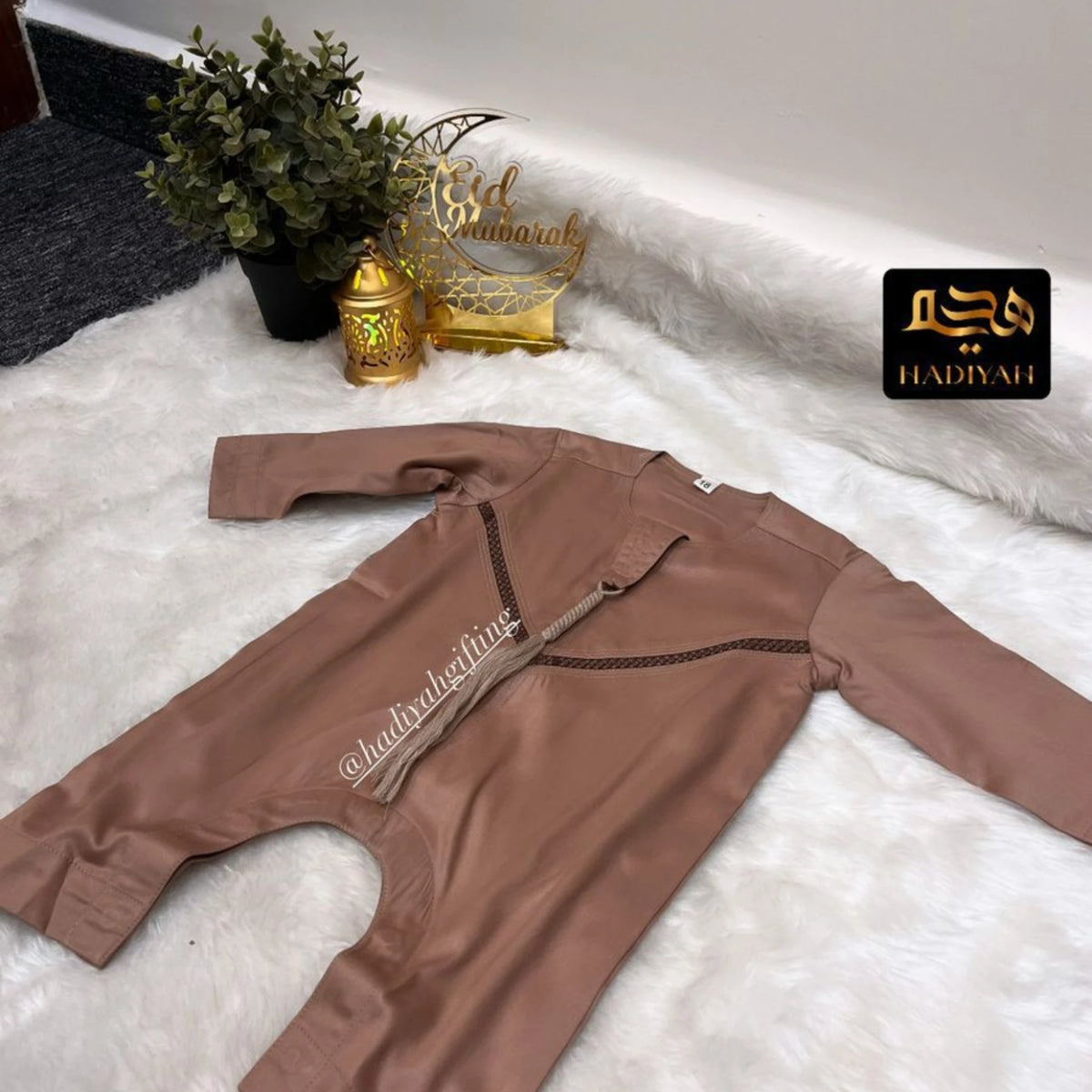 Flat lay of Brown Thobe Romper Boys - Baby Boys Thobe Romper with Eid decor, showcasing elegant stitching and premium cotton blend fabric.
