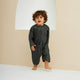 Child wearing a dark gray outfit standing against a plain background