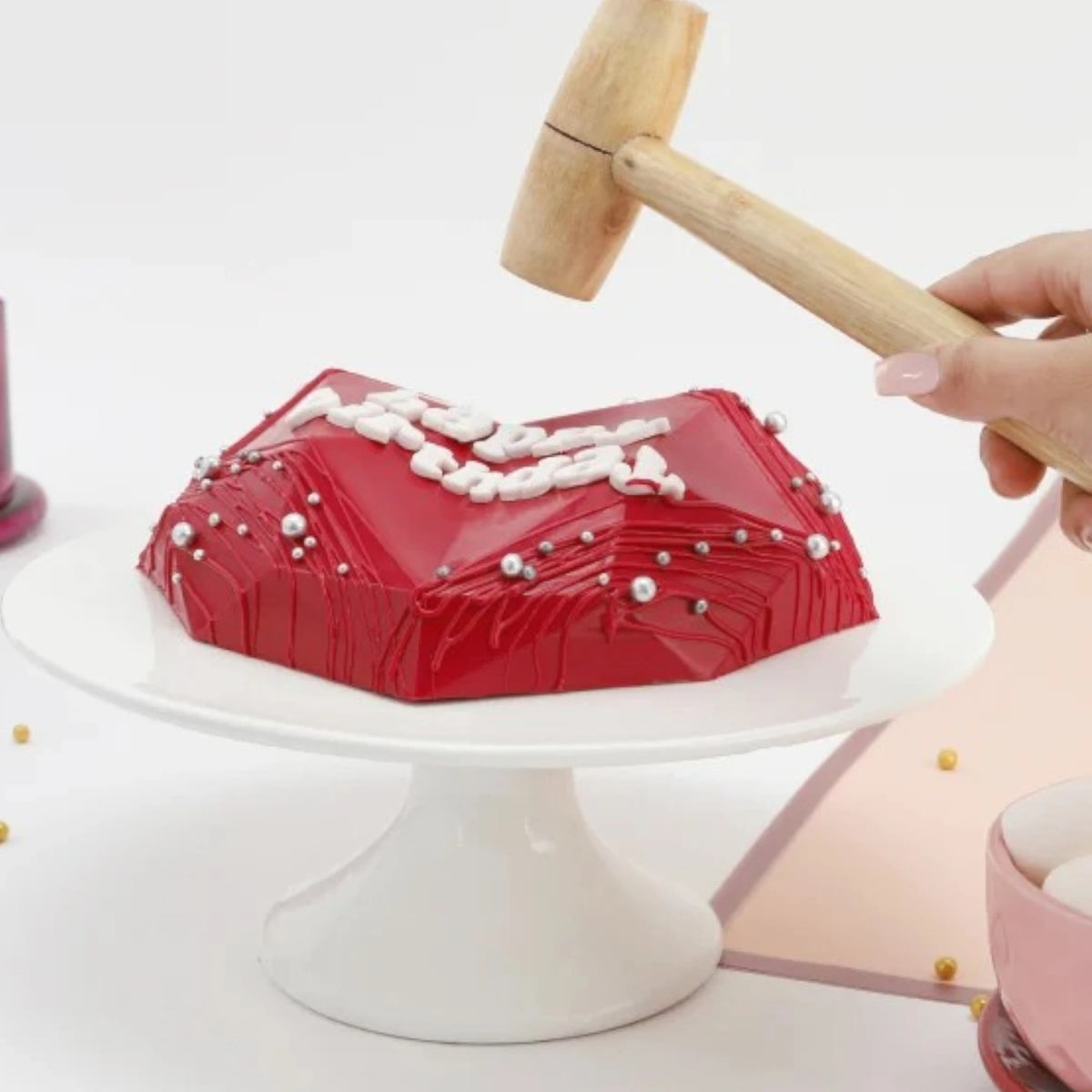 Red Velvet Pinata Cake being cracked open with wooden hammer, revealing surprise inside, fun birthday treat in heart shape.