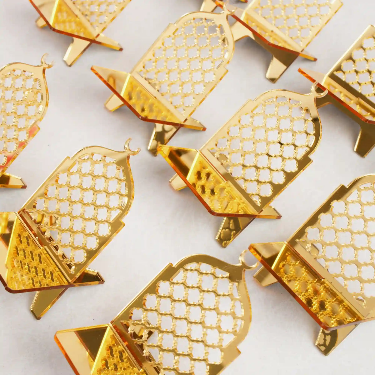 Multiple empty crescent-shaped gold acrylic date stands featuring an intricate lattice design and top crescent moon, arranged in neat rows on a plain white surface.
