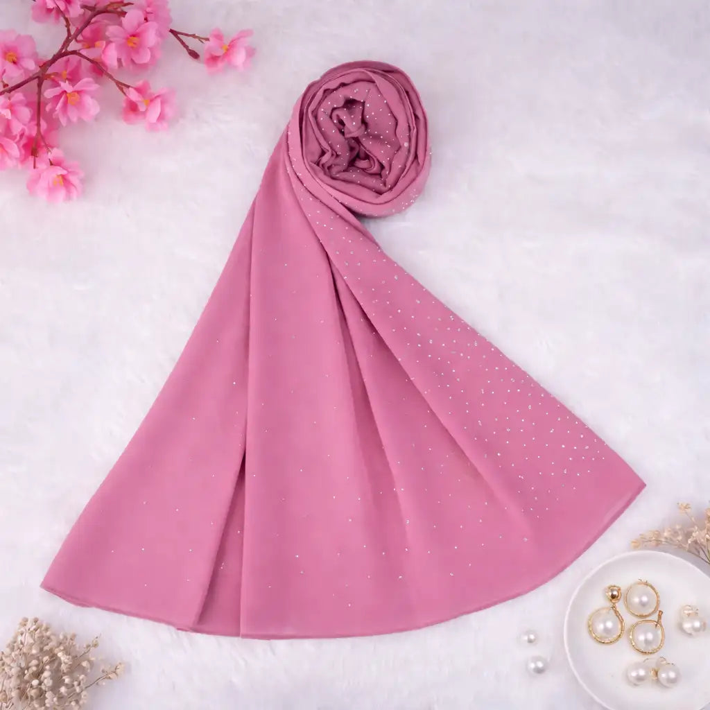 Dark pink studded hijab rolled and displayed on a white surface with floral and pearl accents. Perfect chiffon scarf for elegant modest wear.