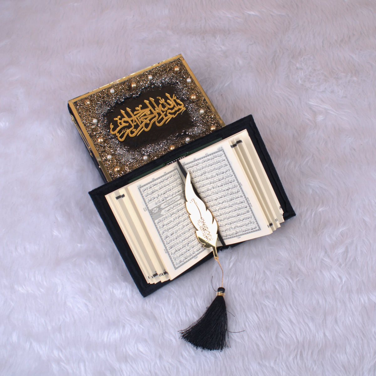 Open Mini Tilawat-e-Quran with gold feather bookmark inside a black velvet designer box, part of the Black Sequence Collection for religious gifting.
