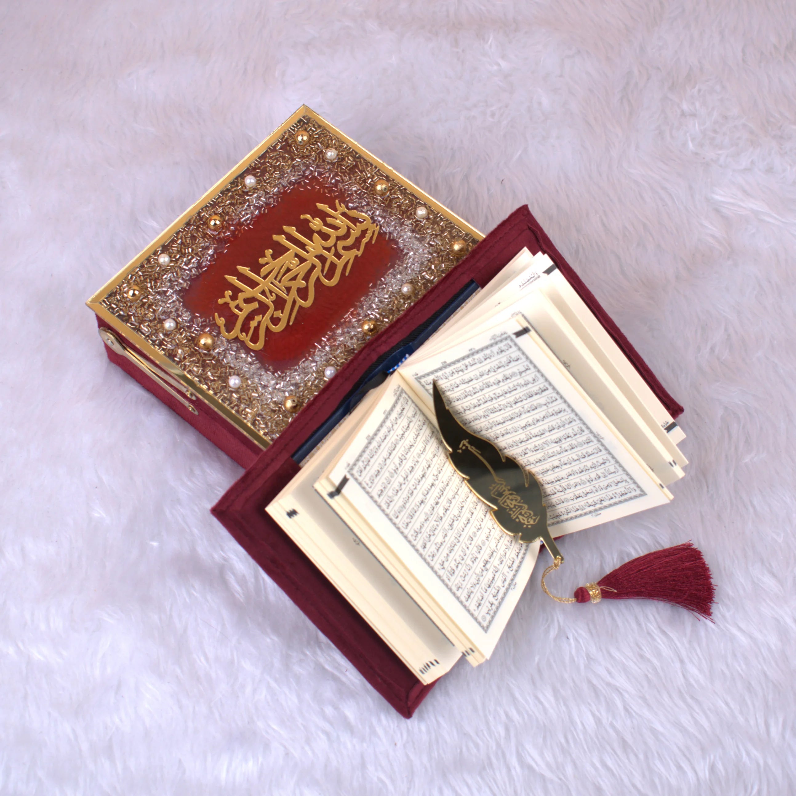 Open Maroon Mini Velvet Quran Set showing Arabic script pages, gold feather bookmark, and embellished designer box. Perfect ceremonial gift item.