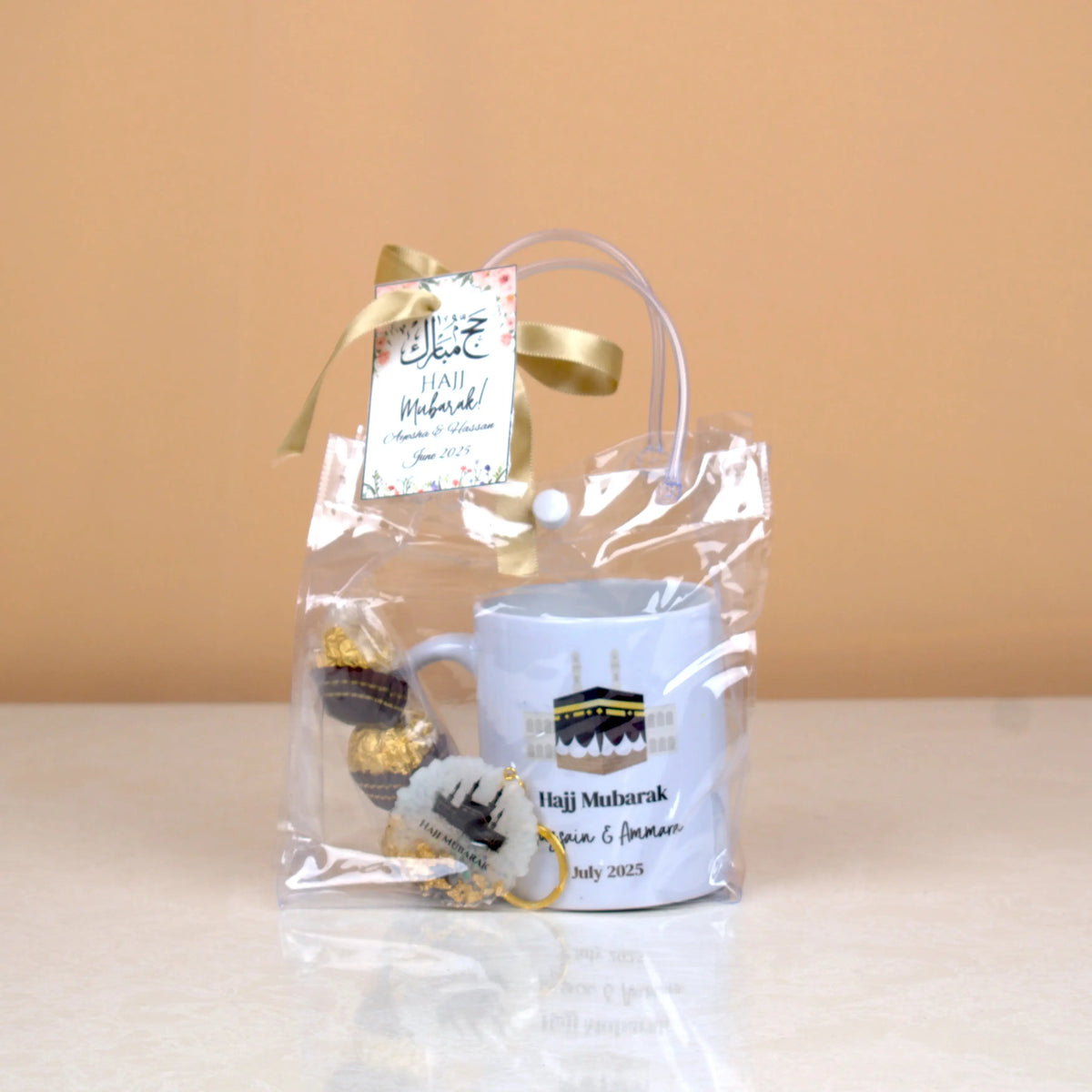 Barakah Blessings Hamper in clear pouch with ribbon, Hajj Mubarak tag, mug, keychain, and chocolates. Elegant Hajj gift for loved ones.