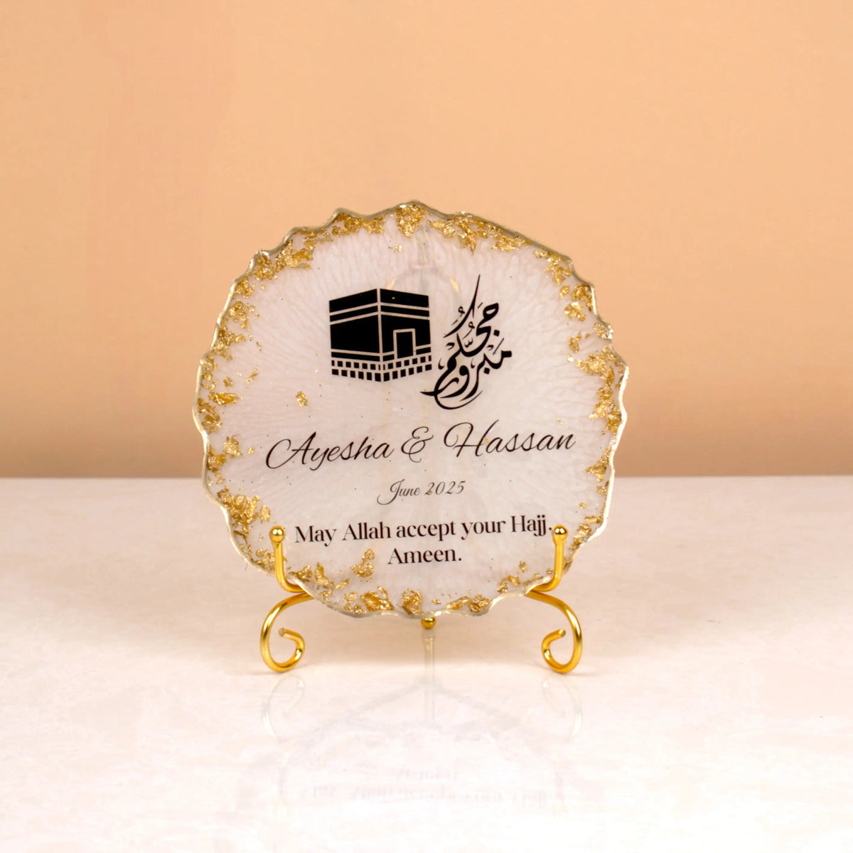 Close-up of personalized Hajj frame with Kaaba artwork and gold stand from Makkah Moments Hamper. Elegant Islamic decor gift item.