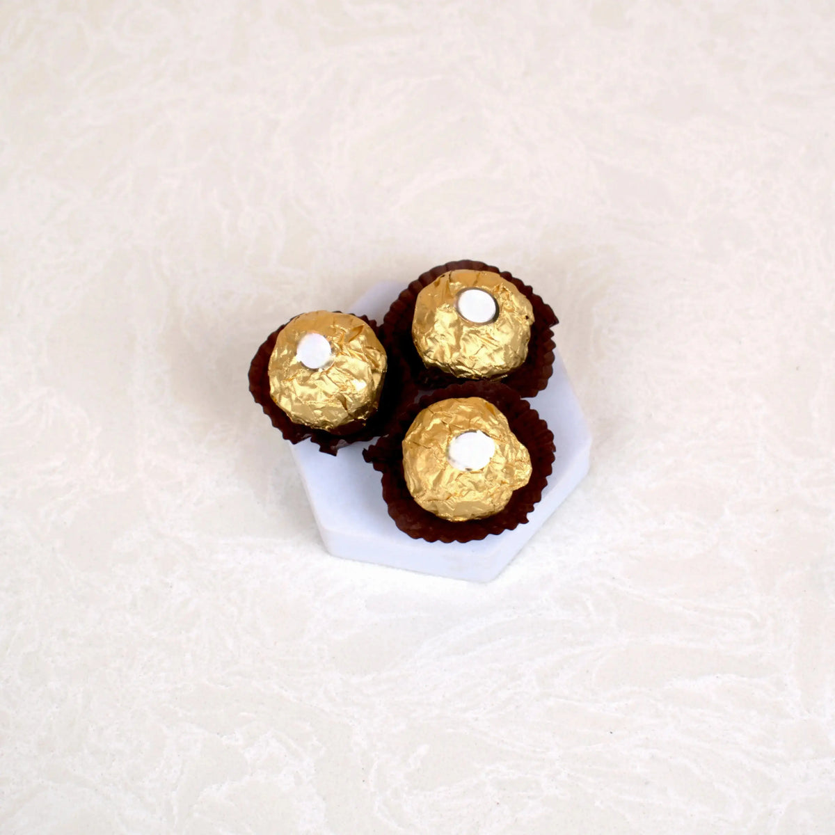 Three Ferrero Rocher chocolates on a hexagonal tray, part of the Makkah Moments Islamic Gift Hamper. Sweet addition to ceremonial gifts.