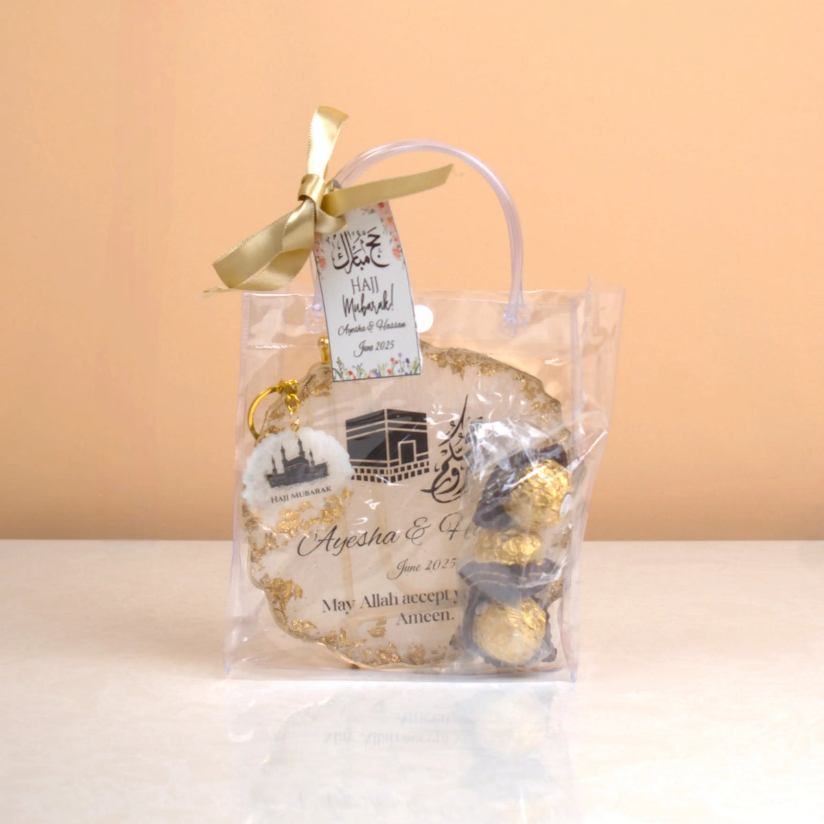 Makkah Moments Hamper packaged in a clear gift bag with ribbon, includes personalized Hajj frame, chocolates, and keychain. Great for gifting.