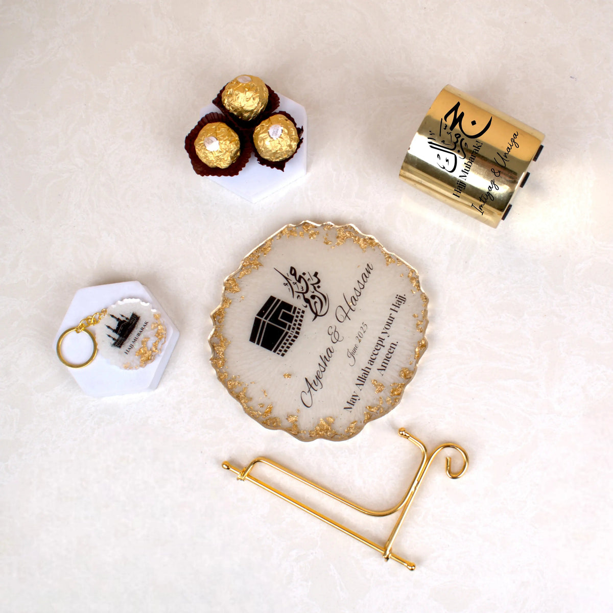 Flat lay of Jannah Journey Hamper - Gift of Faith & Blessings with Hajj frame, Ferrero Rocher chocolates, gold candle, and Kaaba keychain.