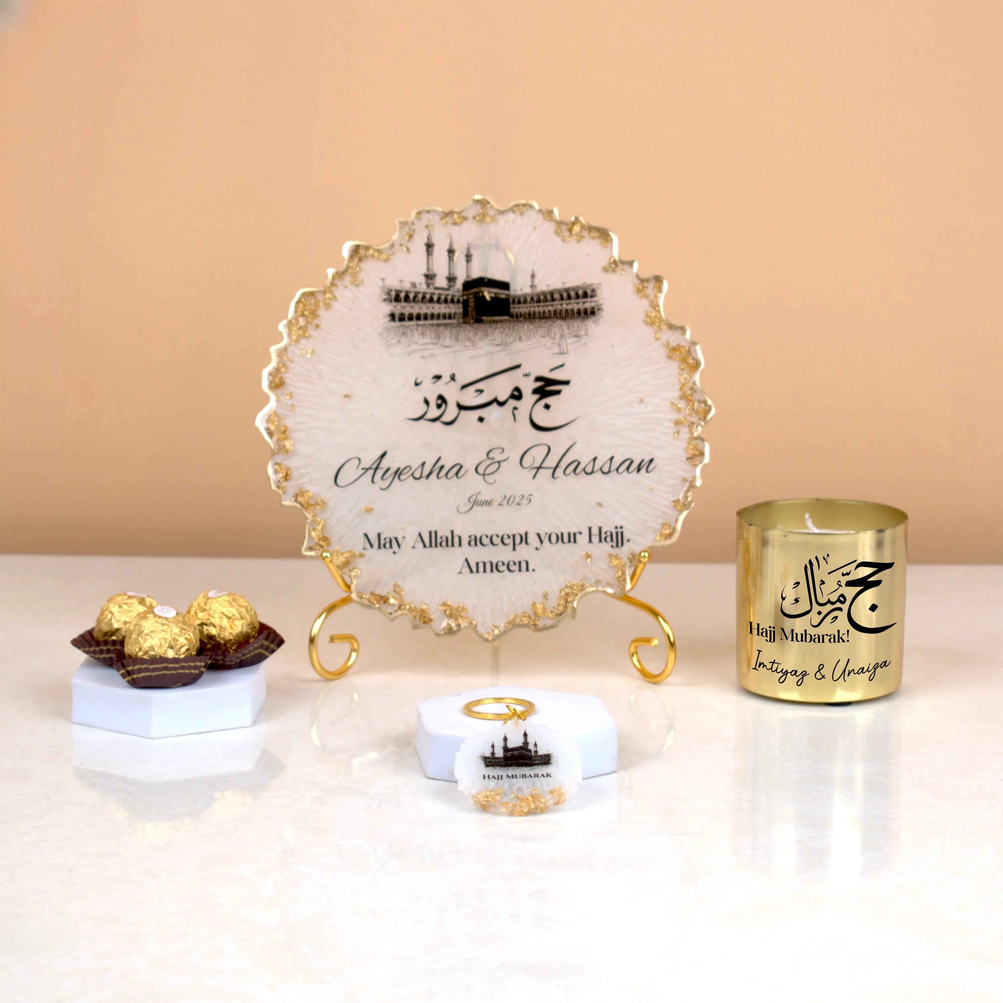 Jannah Journey Hamper - Gift of Faith & Blessings featuring a personalized Hajj frame, gold candle, chocolates, and keychain on display stand. Main image