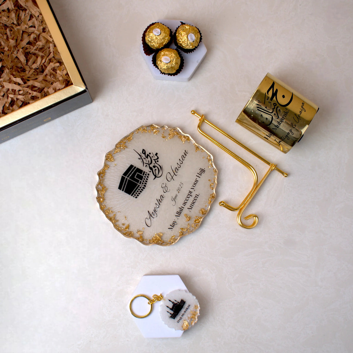 Unboxed Pilgrim's Promise Hamper showing Hajj Mubarak candle, Kaaba frame with gold stand, chocolates, and keychain on a white surface.