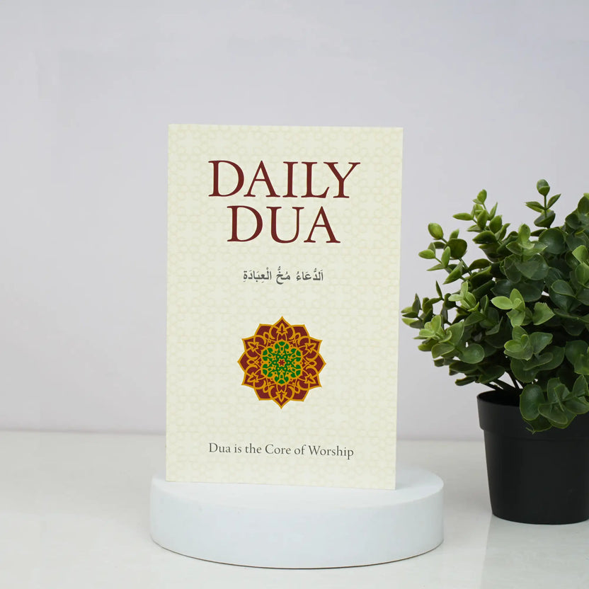 Book titled 'Daily Dua' with a decorative cover on a white surface next to a potted plant. Main image