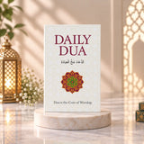 Book titled 'Daily Dua' with a decorative cover on a white surface next to a potted plant.