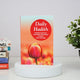 Book titled 'Daily Hadith' with a tulip design on a white surface with books and a plant in the background.
