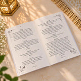 Open book with printed text on a light surface, with a plant in the corner.