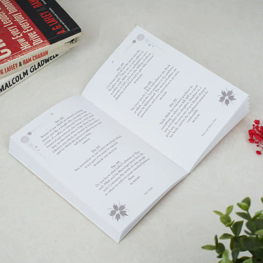 Open book with printed text on a light surface, with a plant in the corner.