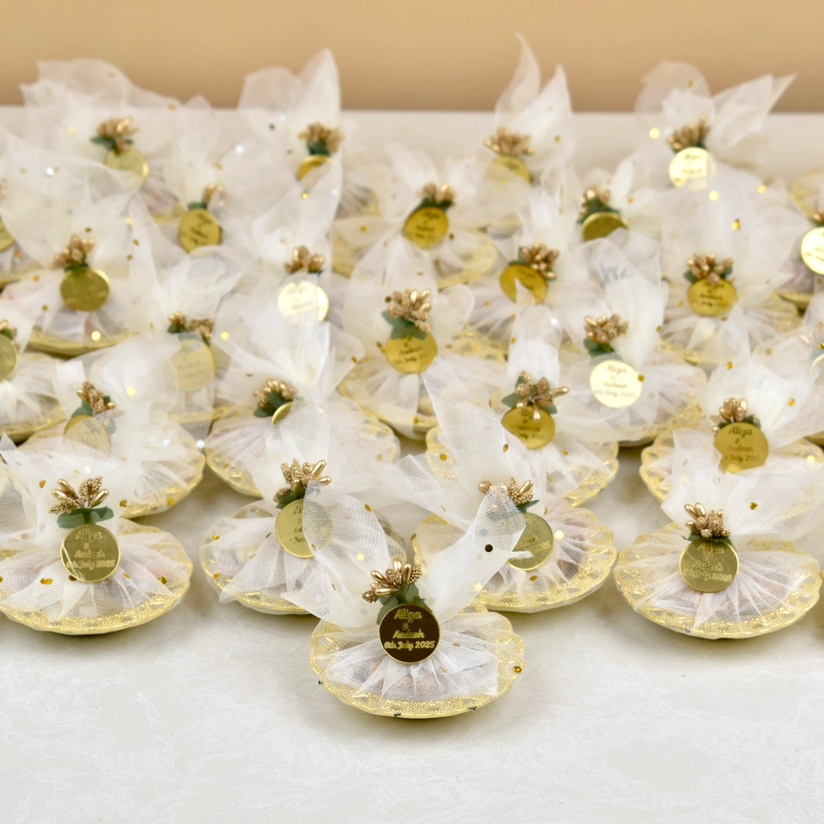 Bulk Mix Dry-Fruit Nikah Favor Gift Trays arranged for a wedding, each wrapped in white mesh with custom gold tags and golden embellishments.