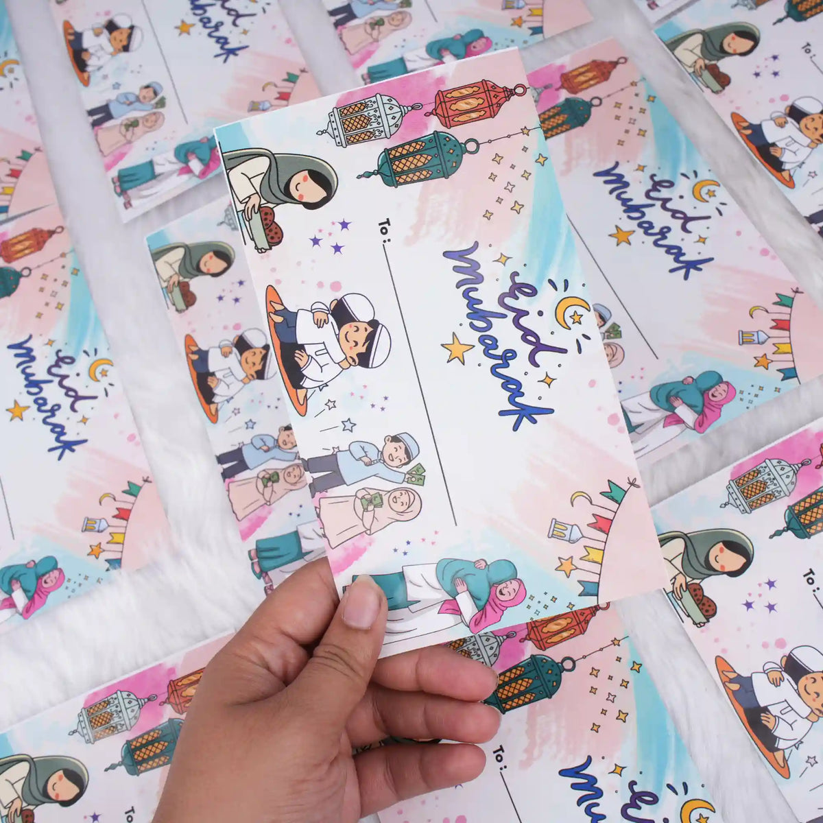 A close-up of a hand holding a white printed Eid Mubarak cash envelope with colorful cartoon characters and hanging lanterns, set against a background of multiple matching envelopes.