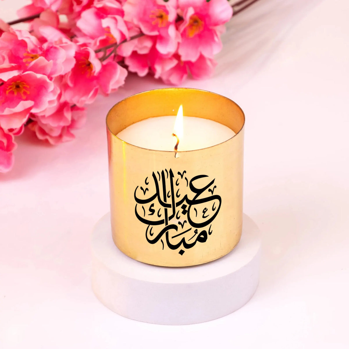 Gold Eid Scented Candle with Arabic calligraphy, lit and styled with pink blossoms. Perfect for Ramadan and Eid home fragrance decor.