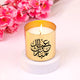 Gold Eid Scented Candle with Arabic calligraphy, lit and styled with pink blossoms. Perfect for Ramadan and Eid home fragrance decor.