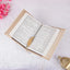 Open book with a decorative gold leaf on a white surface with pink flowers and a gold lantern.