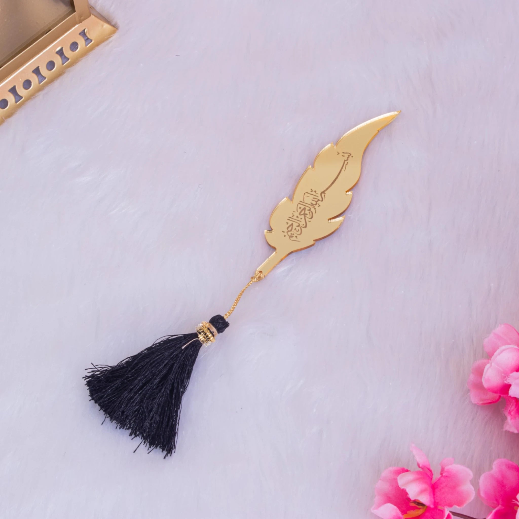 Gold feather-shaped bookmark with black tassel from Black Sequence Tilawat-e-Quran hamper, elegant accessory for Quran reading.
