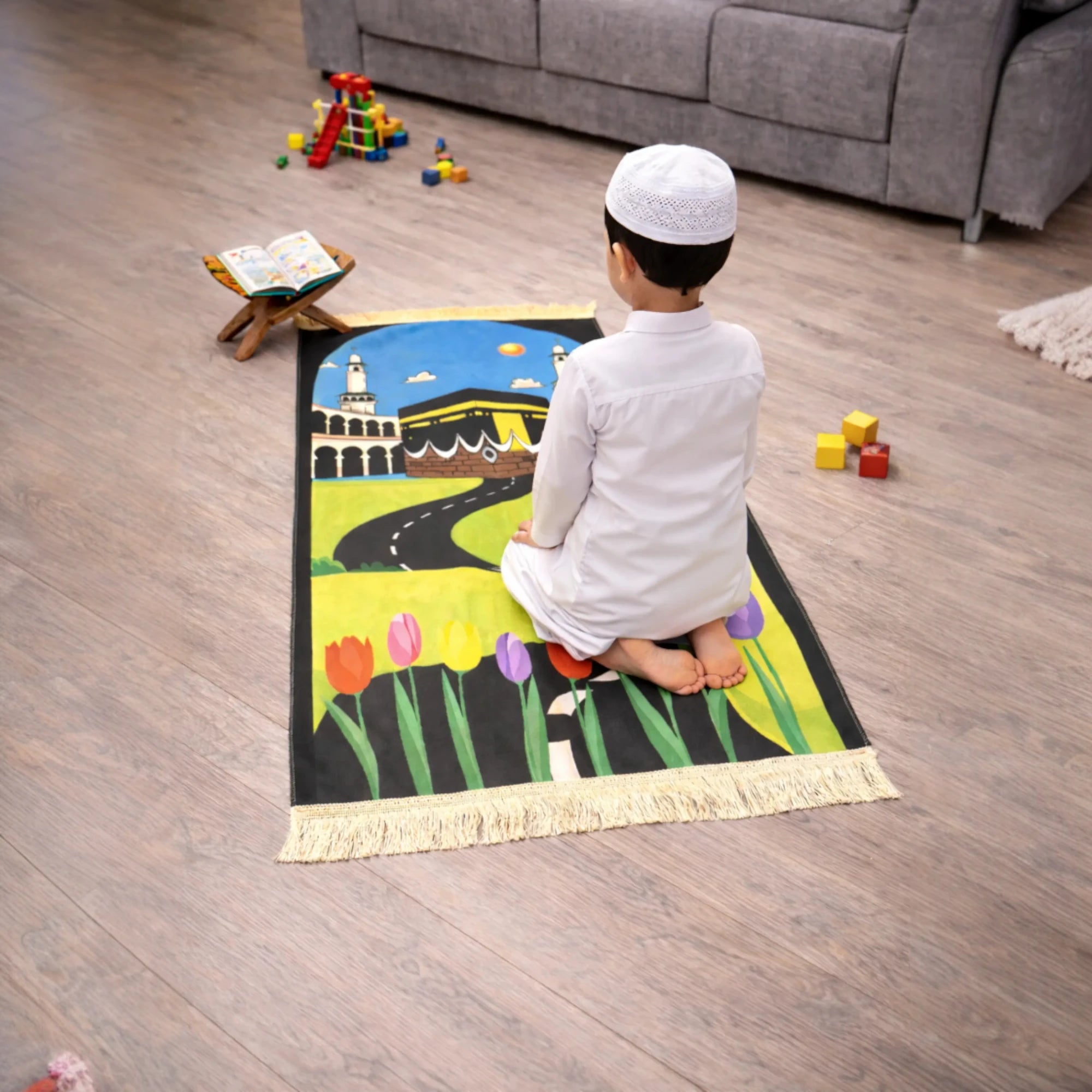 Kids Prayer Mat - Personalized Mat | Janamaz for Kids featuring a child praying on a floral Kaaba-themed mat in a toy-filled room. Main image