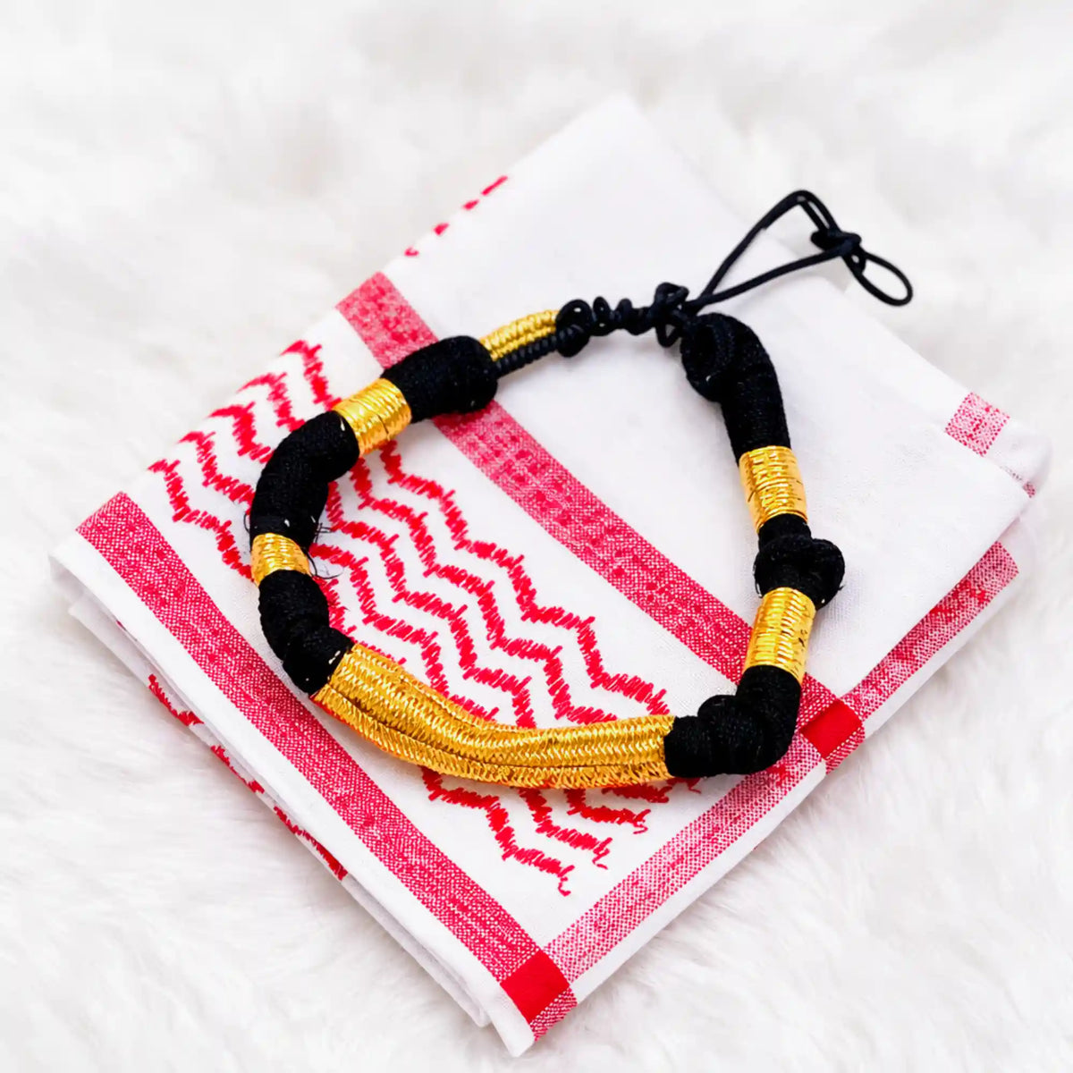 Black and gold beaded bracelet on white fabric with red embroidery, close-up detail