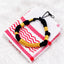 Black and gold beaded bracelet on white fabric with red embroidery, close-up detail