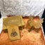 Decorative set with gold butterfly,祈祷文 (prayer text) card, and decorative box on a textured surface.