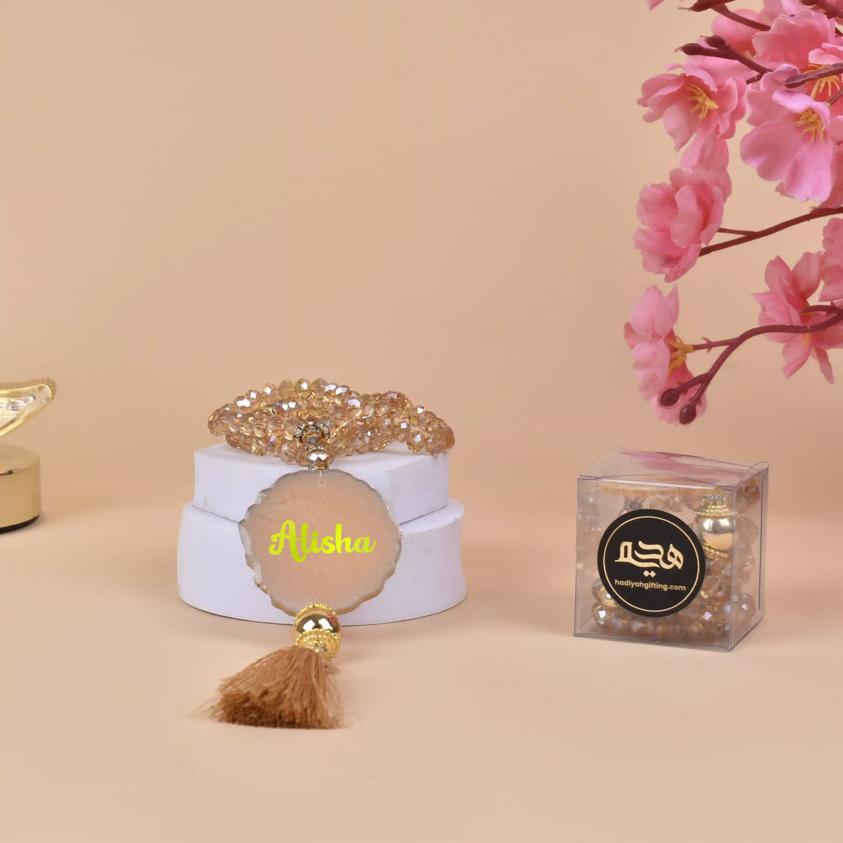 Golden Crystal Tasbeeh - 100 Beads with name 'Alisha', displayed on a white stand with tassel and PVC gift box, ideal for Islamic gifting.