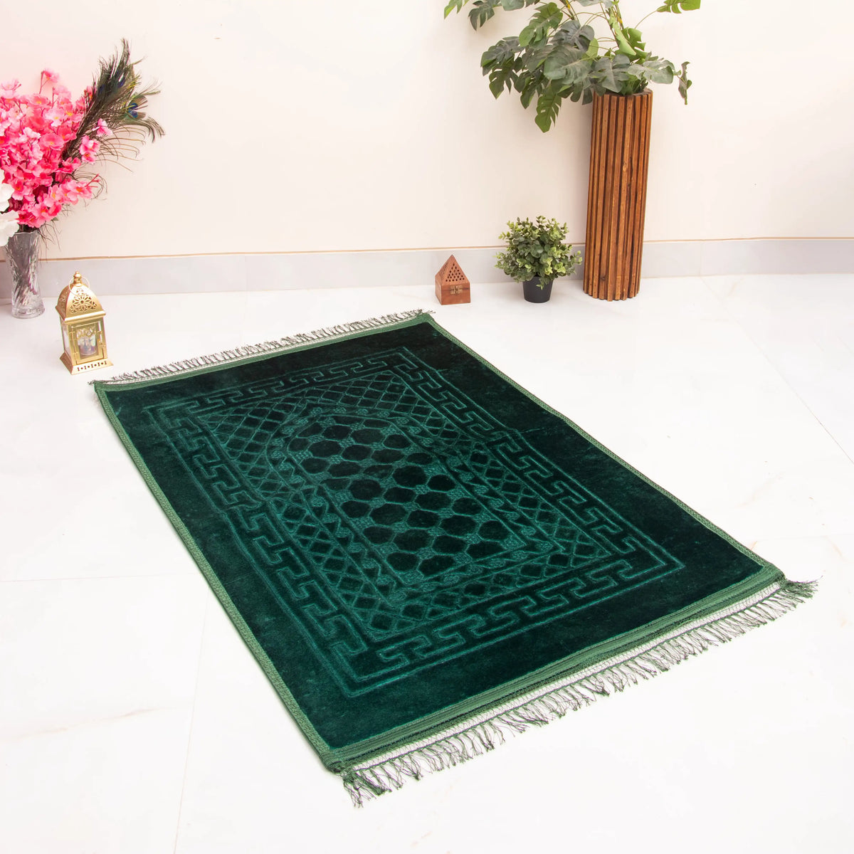Dark green prayer rug with geometric pattern and fringe, laid on white floor. Complements the Green Butterfly Sawab-e-Jariya Gift Set.