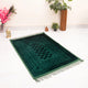 Dark green prayer rug with geometric pattern and fringe, laid on white floor. Complements the Green Butterfly Sawab-e-Jariya Gift Set.