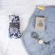Grey Sajdah Serenity Hamper laid out on a white surface, showcasing a grey velvet janamaz, a mini grey velvet Quran, a grey crystal tasbeeh, and a rolled-up blue and white floral prayer makhana.