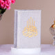 Decorative book with gold calligraphy on a stand, surrounded by flowers and a decorative object.